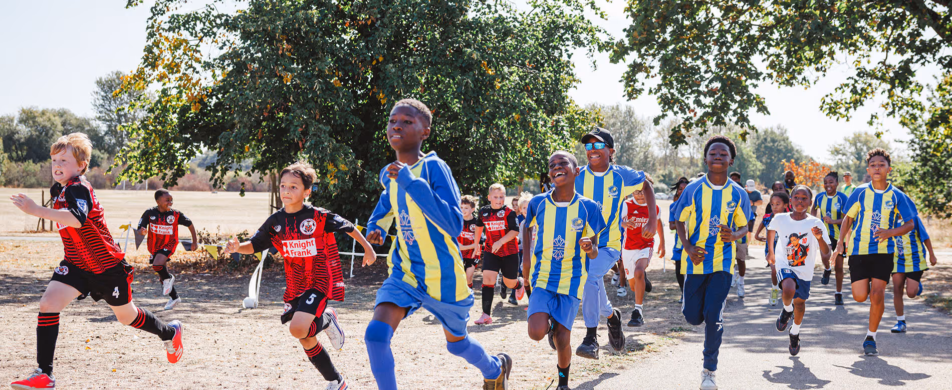 Image shows smiling school children running in a race through a park in South London