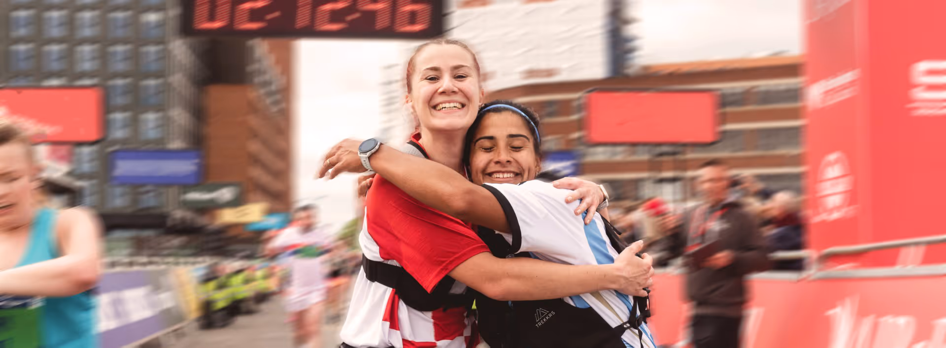 Image shows two happy smiling runners embracing on the finish line