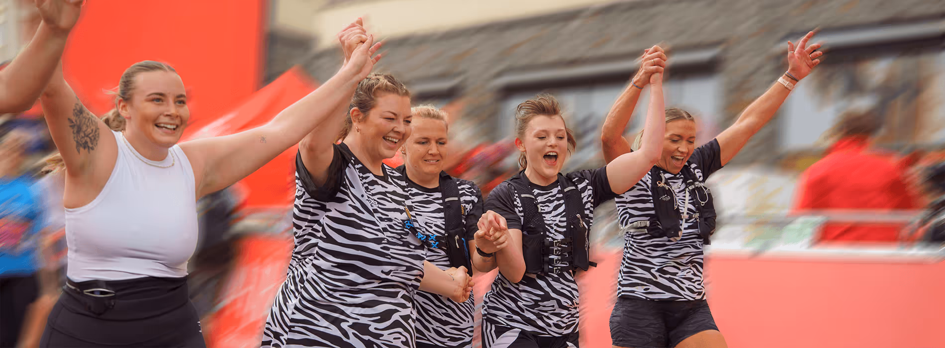 Image shows a group of runners waving their arms and smiling for the camera as they cross the finish line