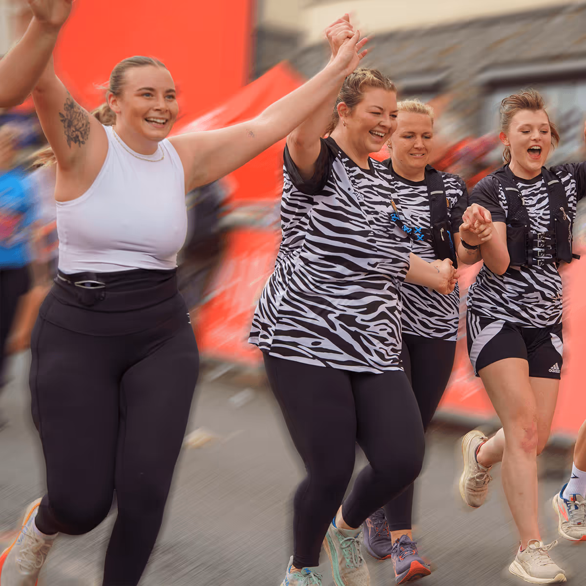 Image shows a group of runners waving their arms and smiling for the camera as they cross the finish line