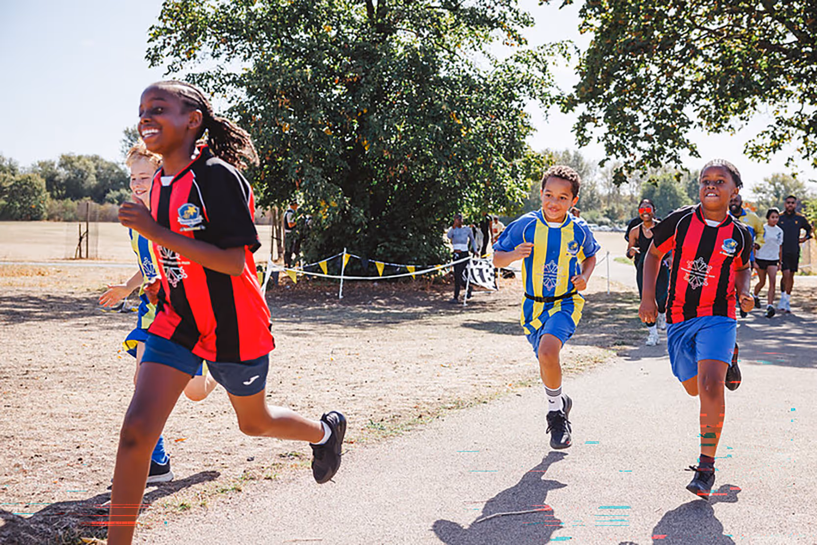 Image shows a smiling young firl and two young boys running in a race in a park.